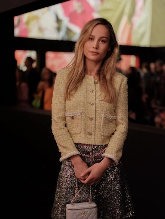 Brie Larson picture standing wearing a yellow top and holding a bag