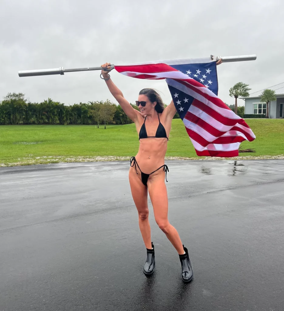 Bryce Adams (@fitbryceadams) Fansly model picture standing on the road holding a american flag. she is wearing black bikini