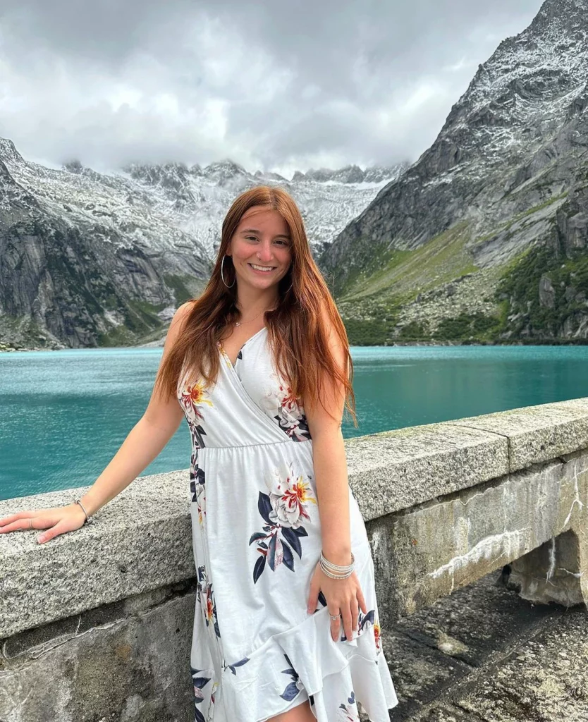 @mikailadancer onlyfans model standing on a stone ledge by a body of water with snow covered mountains