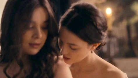 Hailee Steinfeld leaks in the movie Dickinson. She is standing with a woman kissing her shoulder